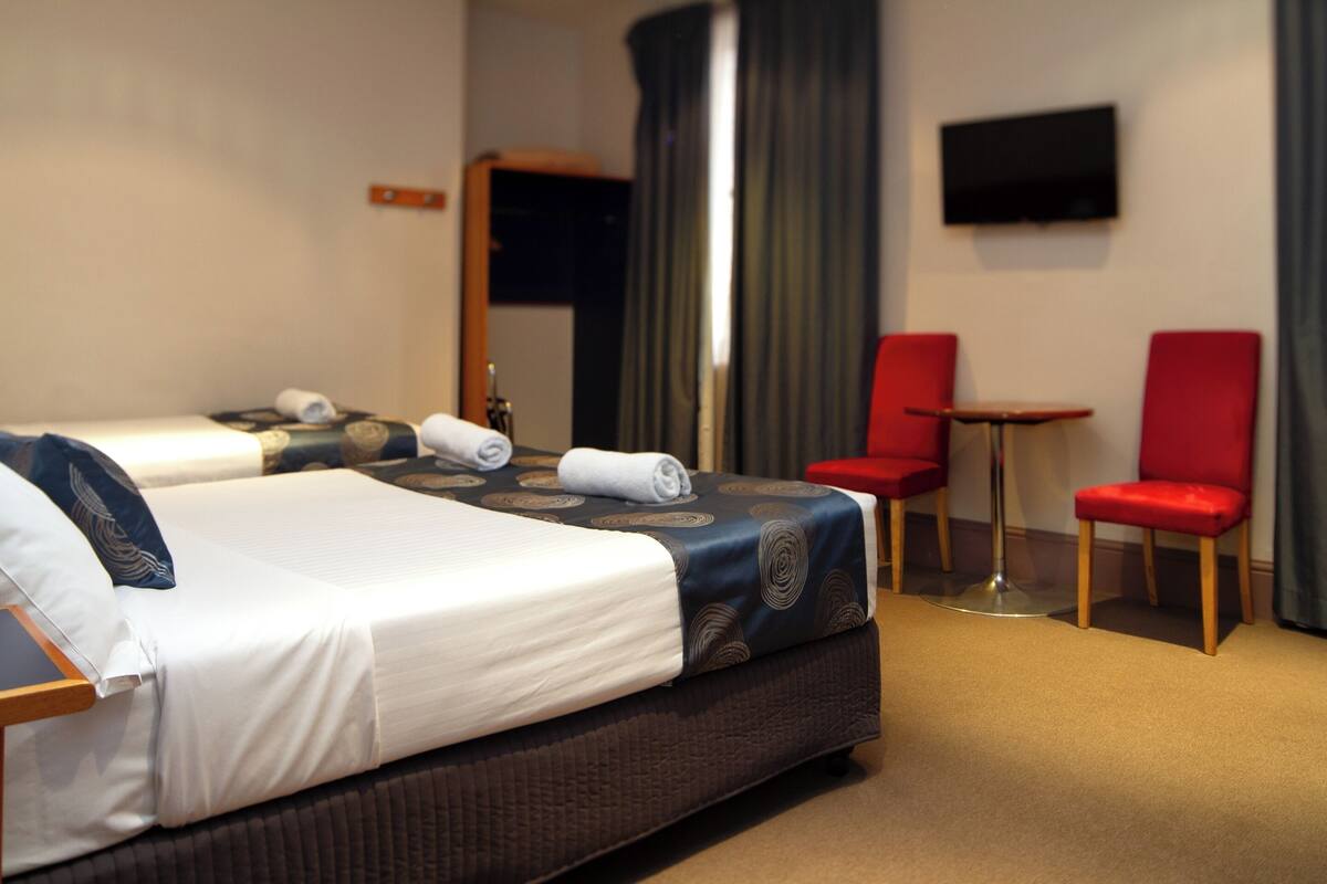 A hotel room with two beds, a TV mounted on the wall, and two red chairs.