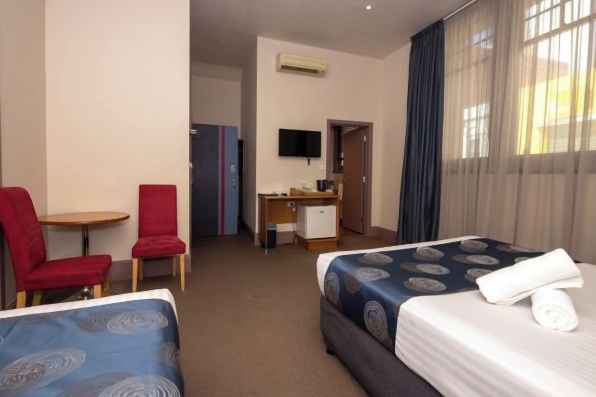 A hotel room with two beds, a desk, a chair, and a TV.