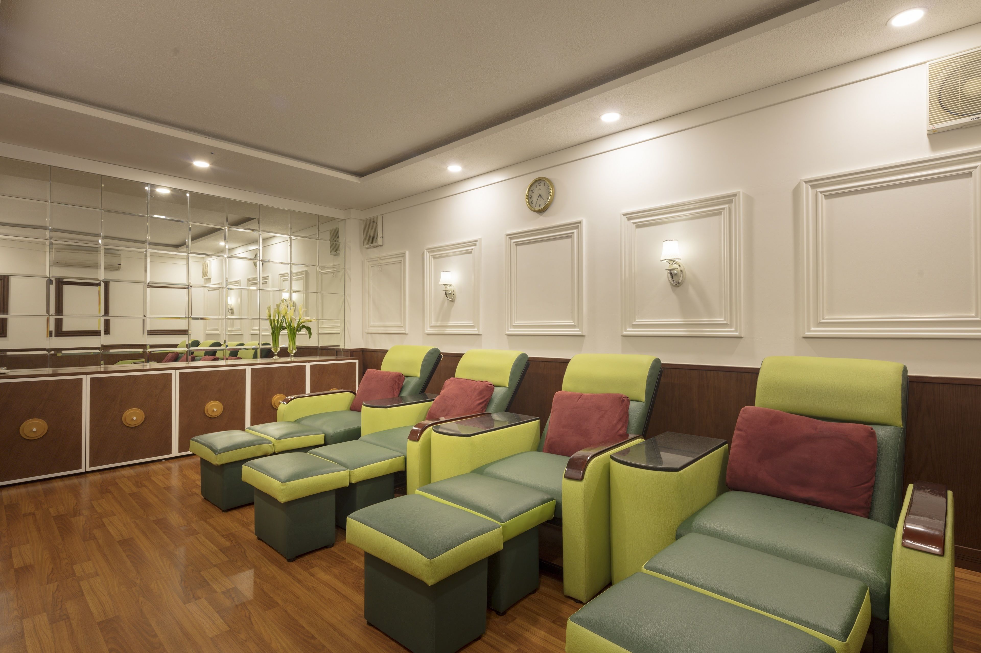 A room with multiple green and yellow massage chairs, a wooden floor, and a mirrored wall.