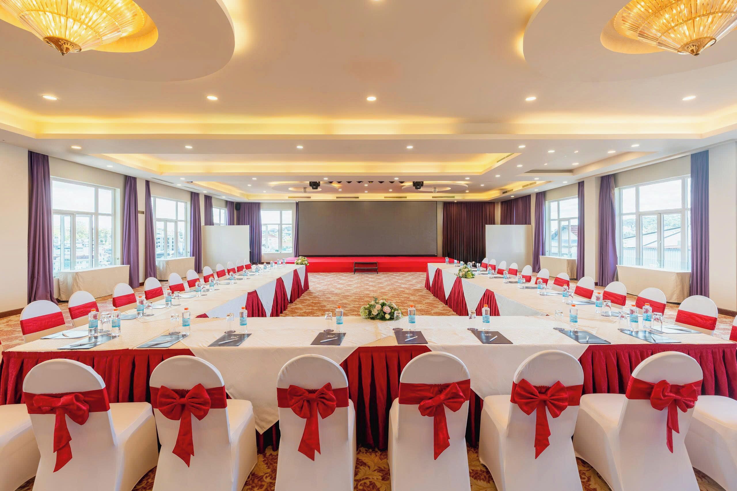 A conference room with a long table, white chairs with red sashes, and a stage at the front.