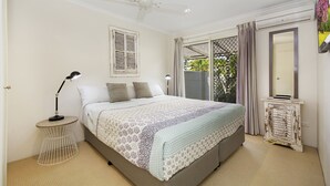 A bedroom with a large bed, a ceiling fan, a bedside table with a lamp, a wardrobe, and a window with curtains. - 44 Cooran Court (Noosa Heads)