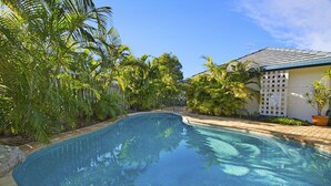 A swimming pool surrounded by lush greenery and a building with a tiled roof. - 44 Cooran Court (Noosa Heads)