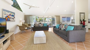 A spacious living room with a flat-screen TV, two sofas, a coffee table, and a large window offering a view of the outdoors. - 44 Cooran Court (Noosa Heads)