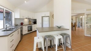A modern kitchen with white cabinets, a central island with stools, a refrigerator, and a dishwasher. - 44 Cooran Court (Noosa Heads)
