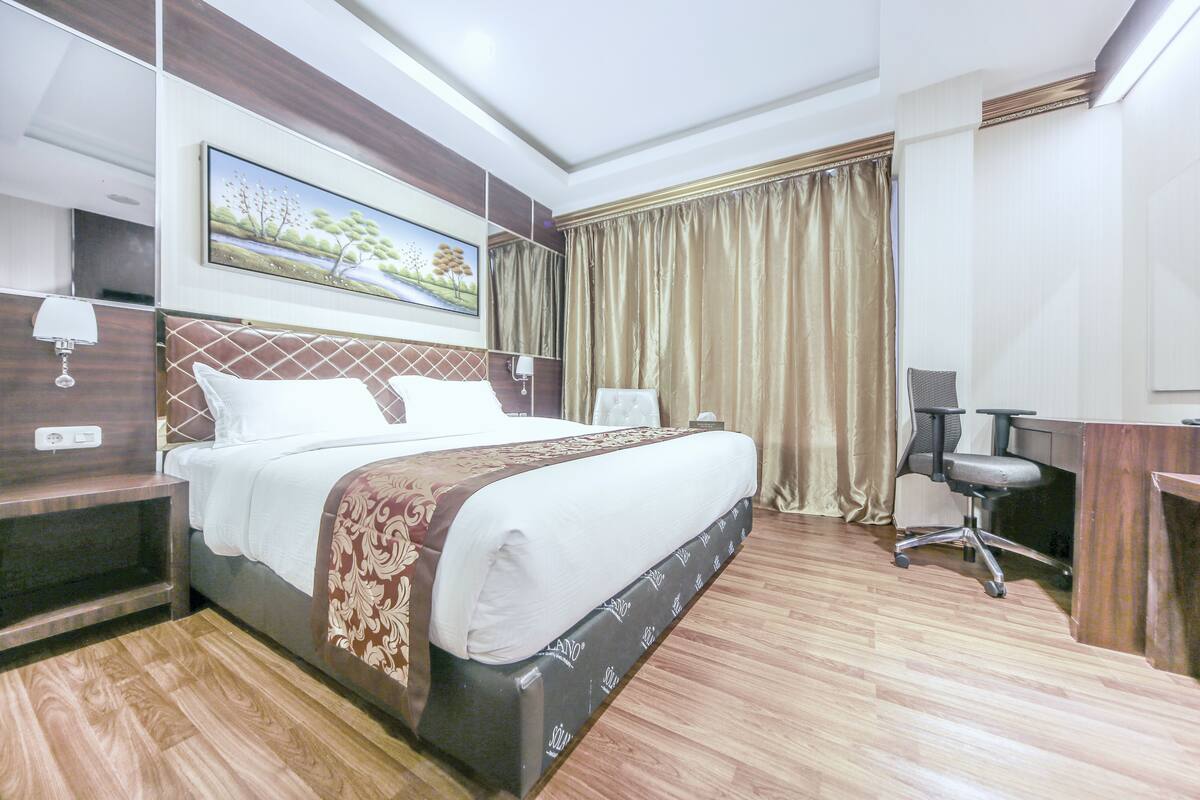 Habitación de hotel con una cama grande, un escritorio, una silla y un cuadro en la pared.