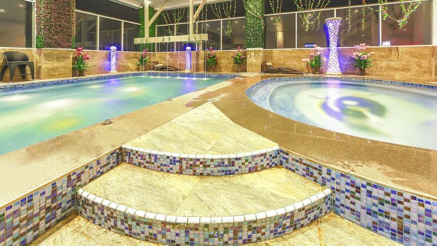 Une grande piscine intérieure avec des marches carrelées menant à l’eau, entourée de murs décorés de plantes et de fleurs.