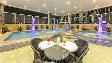 A poolside area with two round tables, chairs, and a small bar area with drinks.