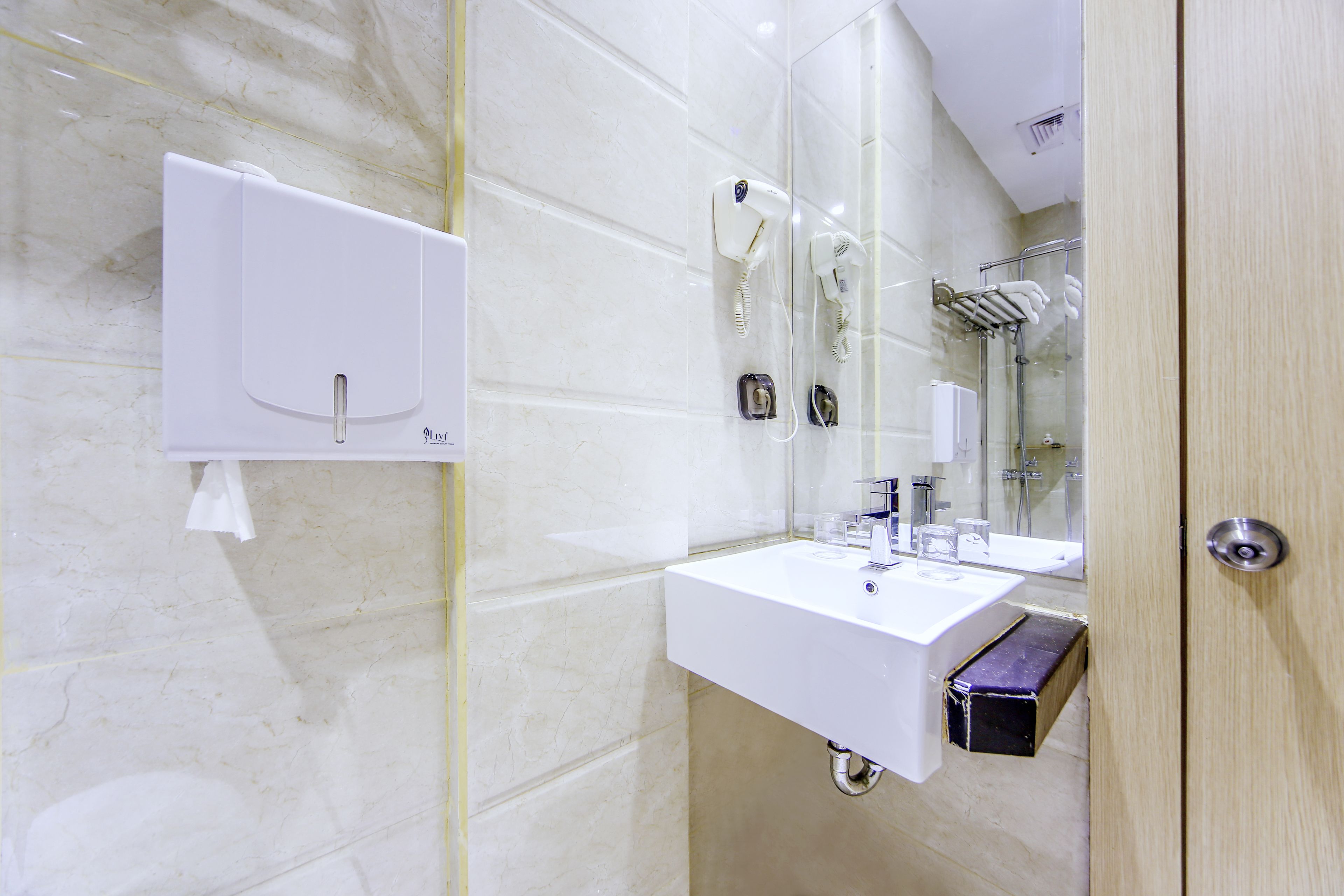 A modern bathroom with a marble wall, a white sink, a mirror, and a towel dispenser.