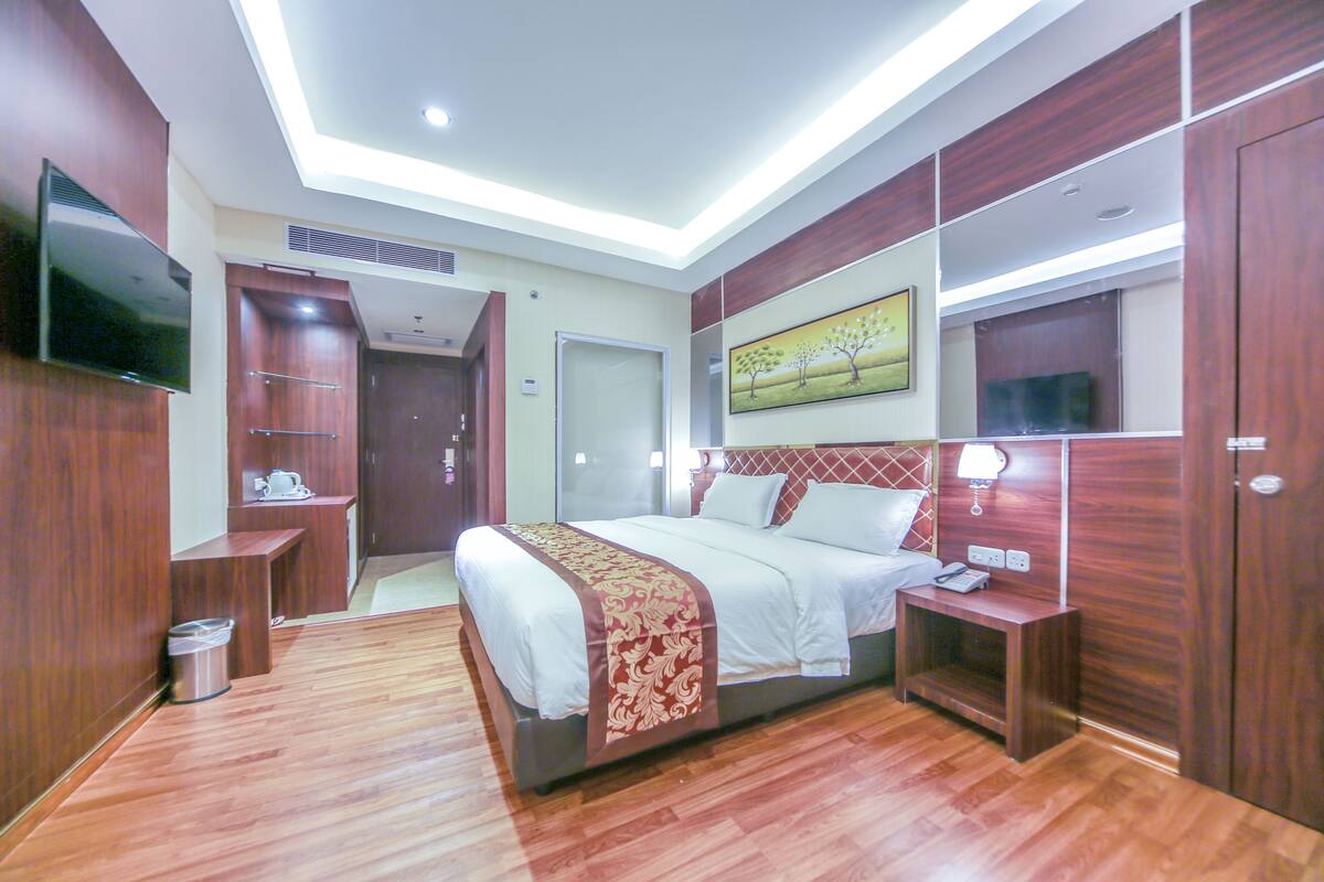 Una habitación de hotel moderna con una cama grande, paneles de madera, un televisor de pantalla plana y un cuadro en la pared.