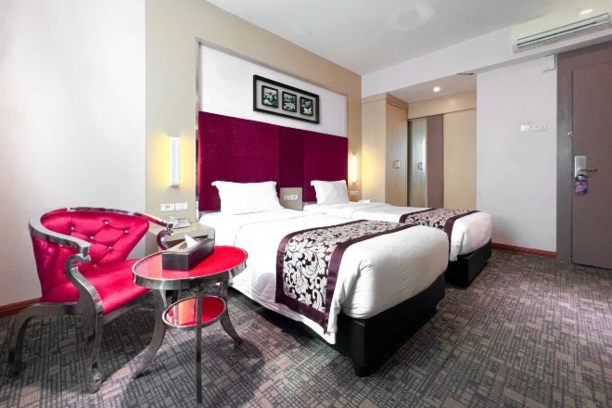 Una habitación de hotel con dos camas, una silla roja, una mesita redonda y un espejo.