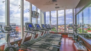 Une salle de sport équipée de tapis de course et de vélos d’exercice, dotée de grandes fenêtres et offrant une vue sur la ville.