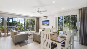 Un vaste espace de vie comprenant une table à manger en bois, des chaises blanches, un canapé et un ventilateur de plafond.