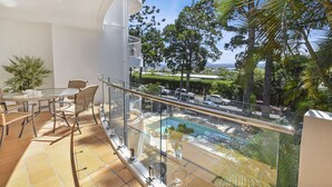 Un balcon doté d’une rambarde en verre, offrant une vue sur une piscine et une végétation luxuriante.