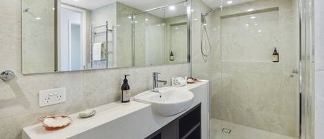 A modern bathroom with a glass-enclosed shower, a white sink, and a large mirror.