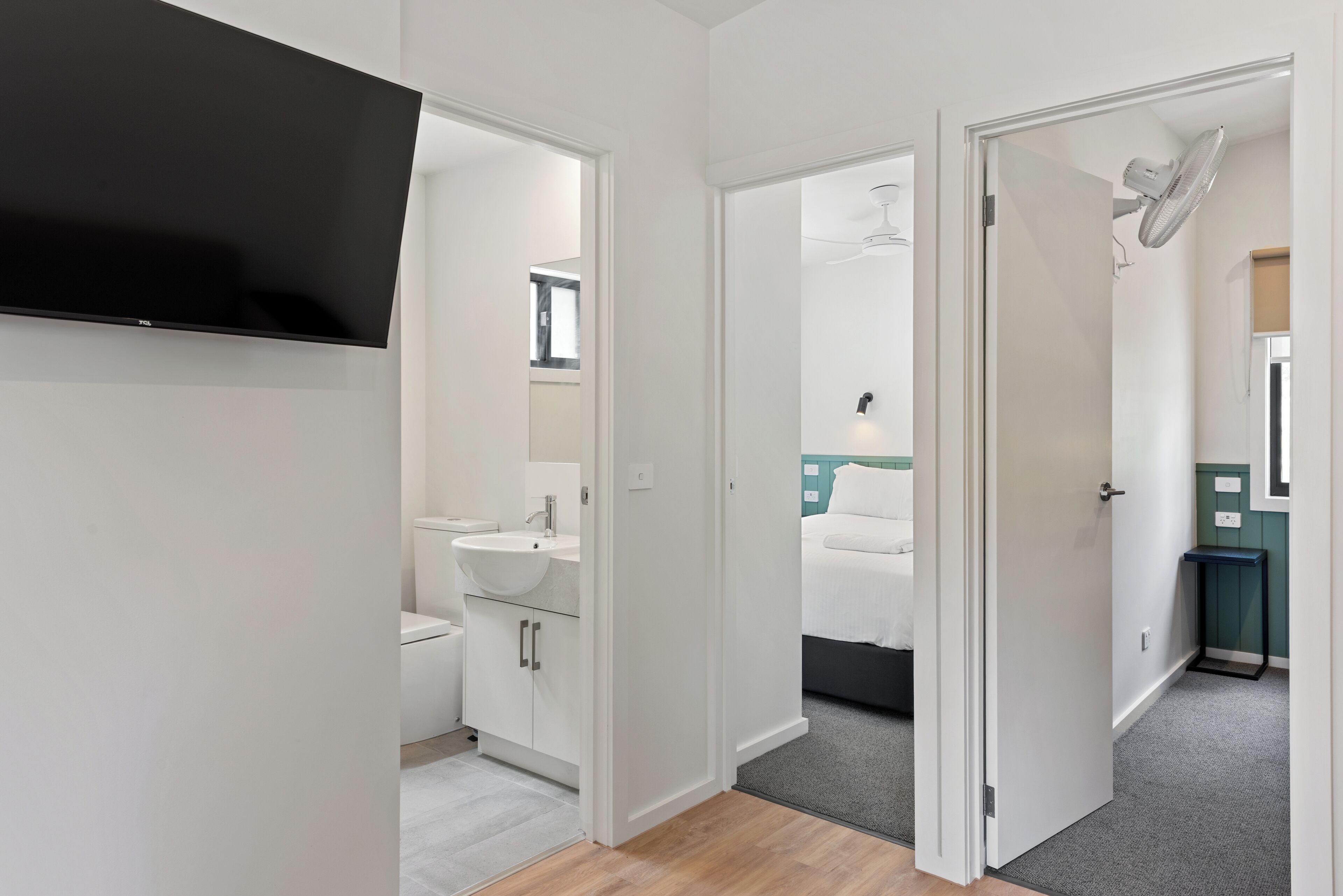 Een moderne hotelkamer met een flatscreen televisie, een badkamer met wastafel en toilet, en een bed met een groen hoofdeinde.