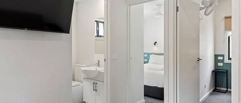 Een moderne hotelkamer met een flatscreen televisie, een badkamer met wastafel en toilet, en een bed met een groen hoofdeinde.