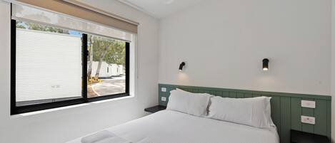 Habitación de hotel con cama, ventilador de techo, ventana con persianas y vistas al exterior.