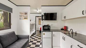 A compact kitchen with a black and white checkered floor, a white refrigerator, a microwave, a sink, and a television mounted above it.