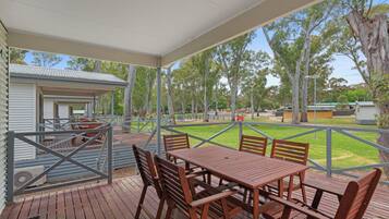 A covered outdoor area with a wooden table and chairs, surrounded by a metal fence and trees.
