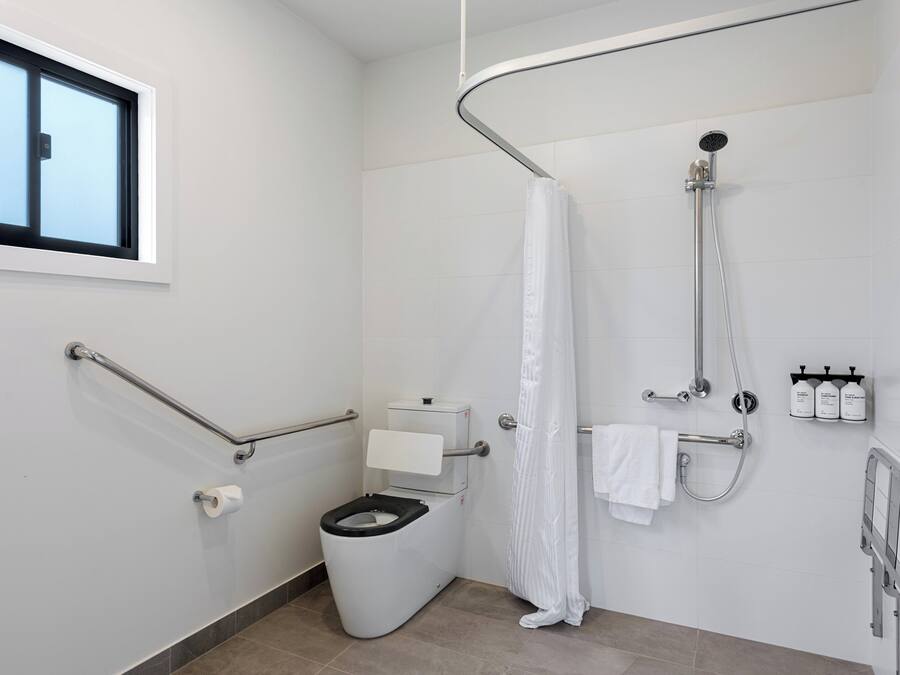 Et moderne badeværelse med toilet, brusebad og gelænder.