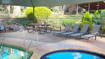 Un área de piscina exterior con un patio techado, sillas de descanso y una mesa de picnic.