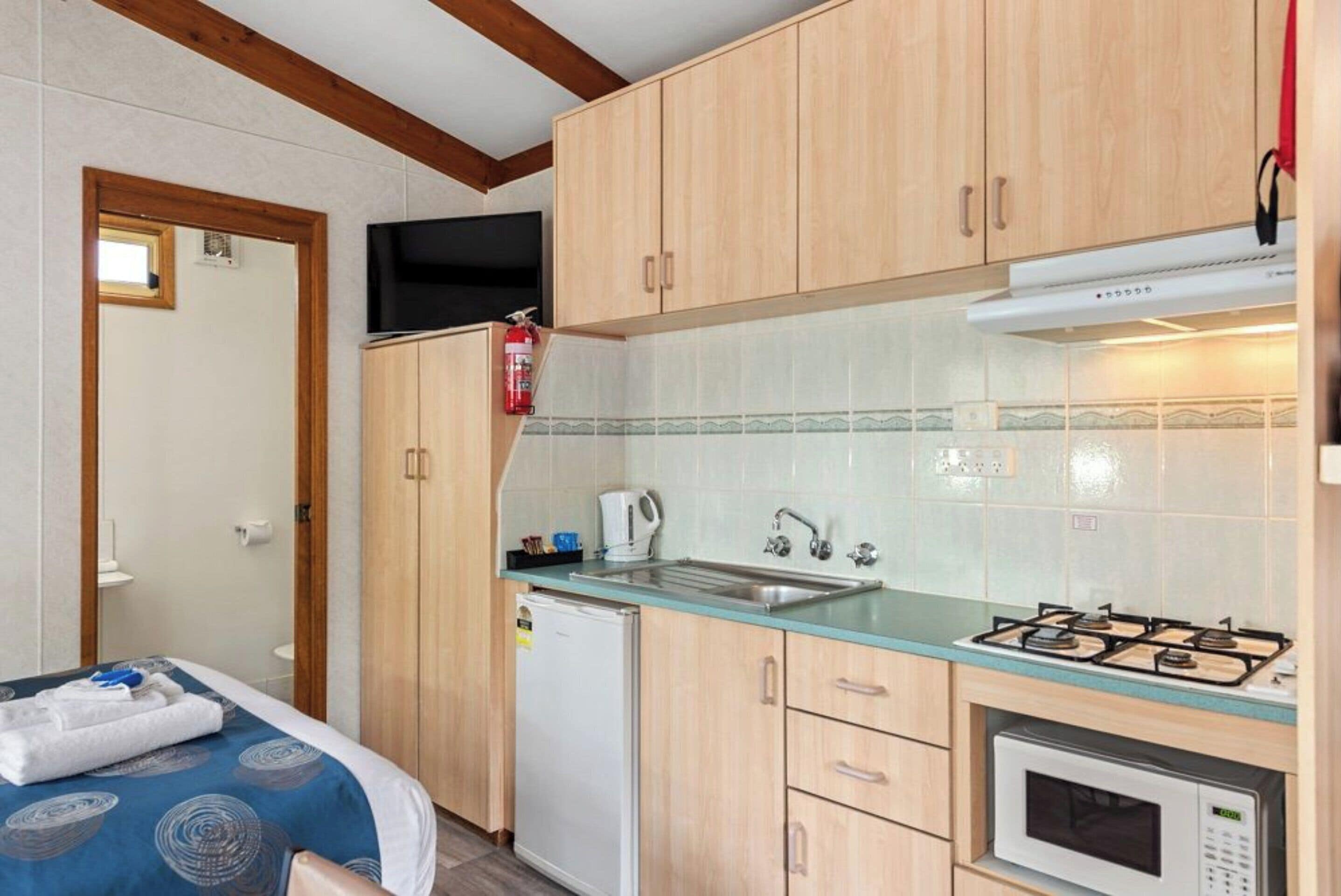 Una cocina compacta con armarios de madera, una estufa a gas, un microondas y un lavamanos.