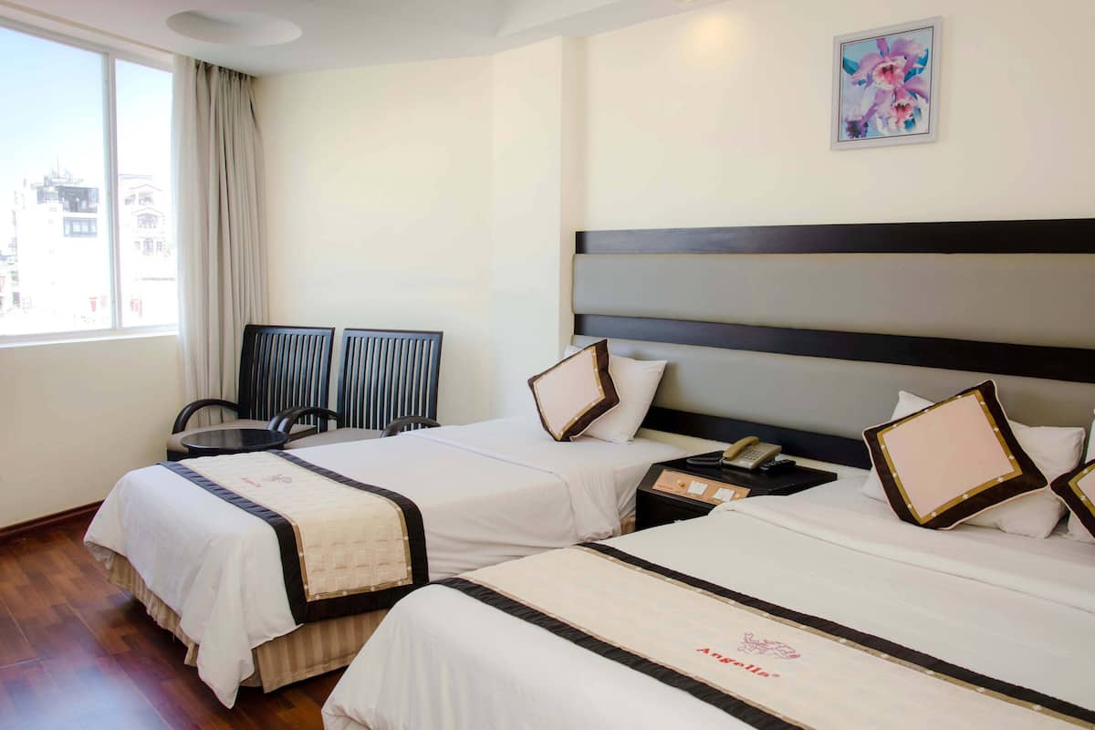 A hotel room with two beds, a small table, chairs, a nightstand, and a window with curtains.