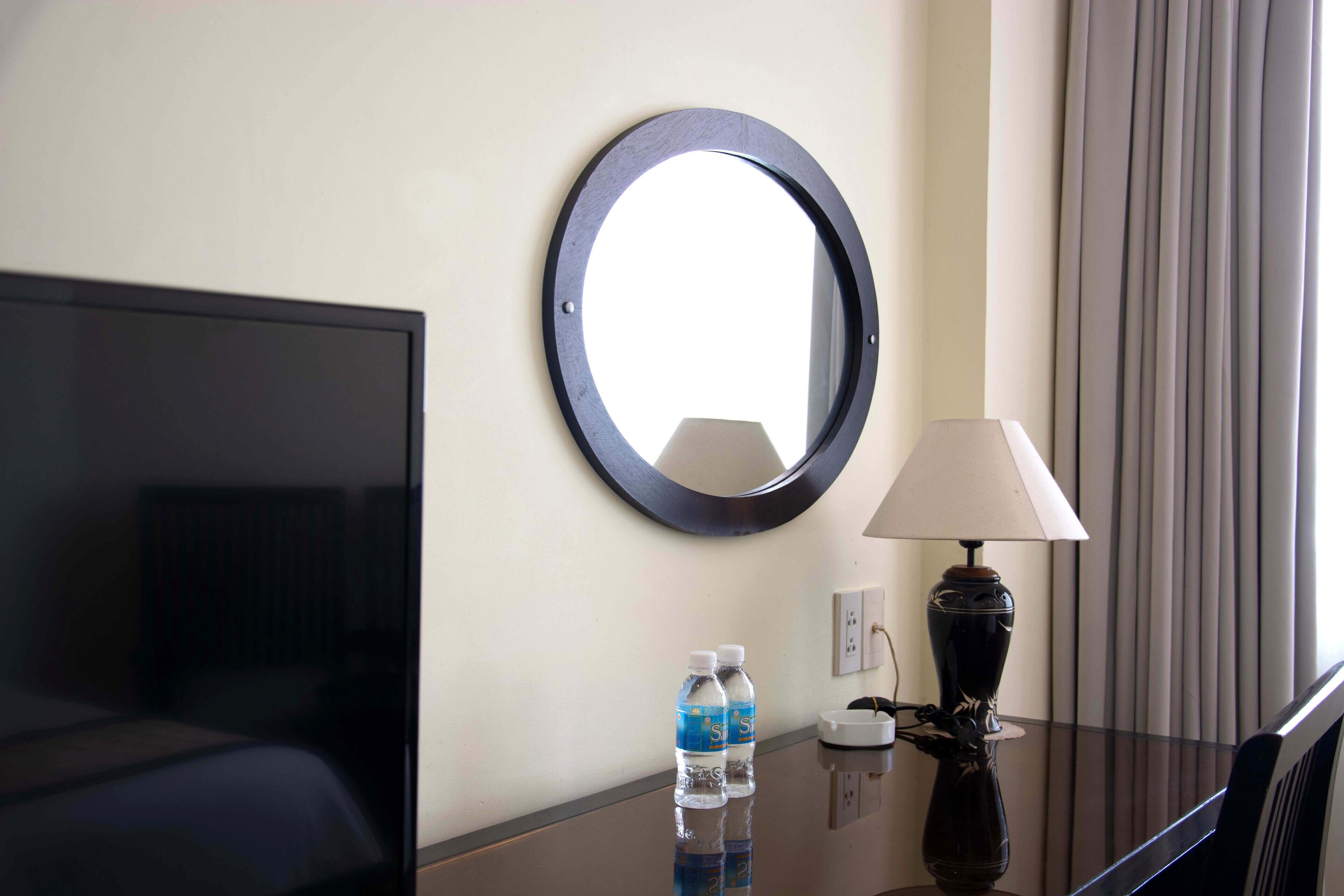 Une chambre d’hôtel avec un lit, une télévision, un miroir rond, une lampe et deux bouteilles d’eau posées sur une table.