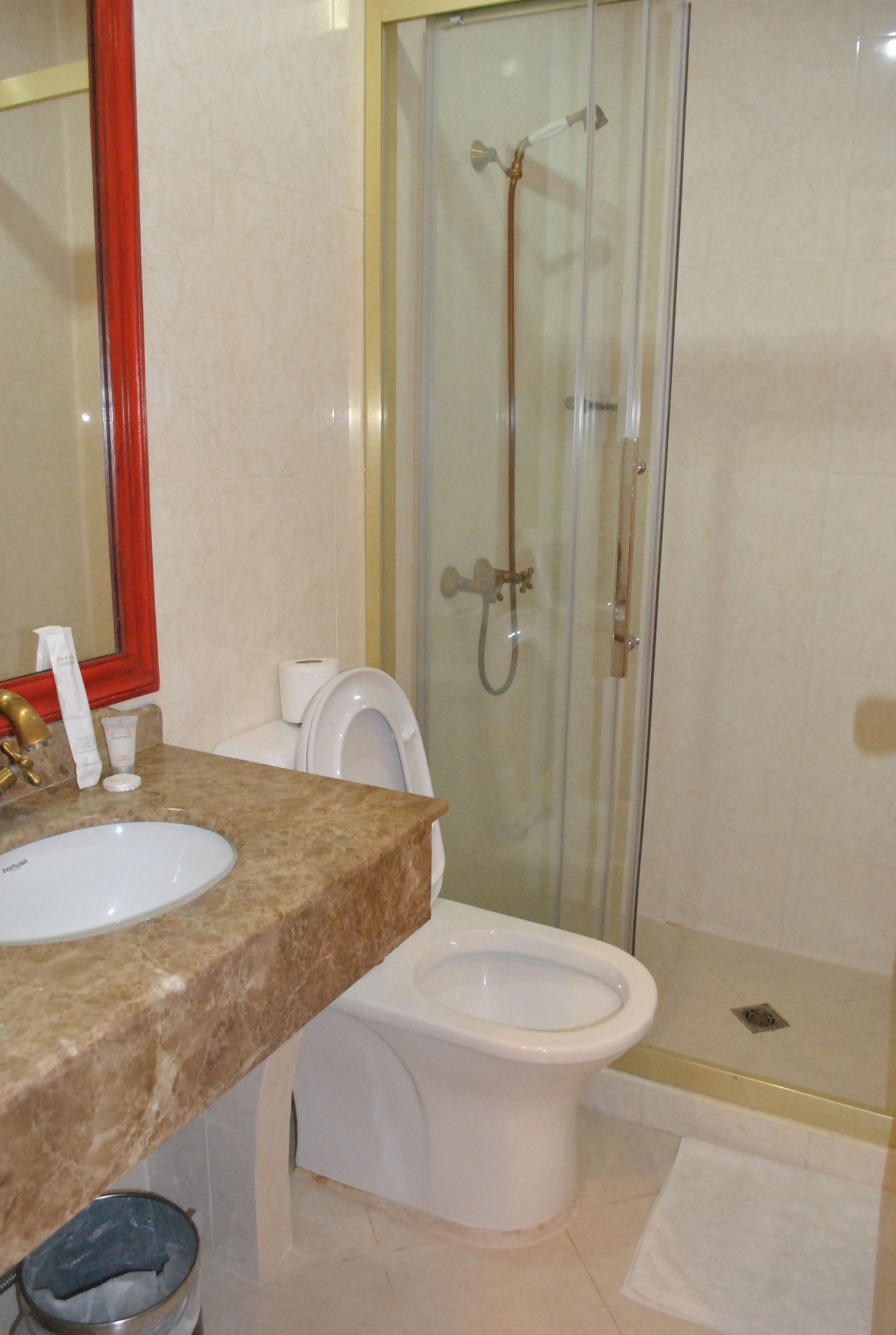 A bathroom with a marble countertop, a white sink, a toilet, and a glass-enclosed shower area.