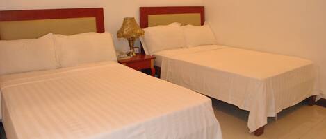 Dos camas individuales con ropa de cama blanca, cabeceros de madera y una mesita de noche con lámpara.