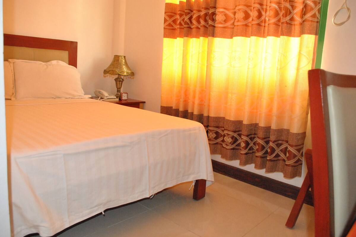 A neatly made bed with a white bedspread, a bedside lamp, and a telephone on a nightstand.