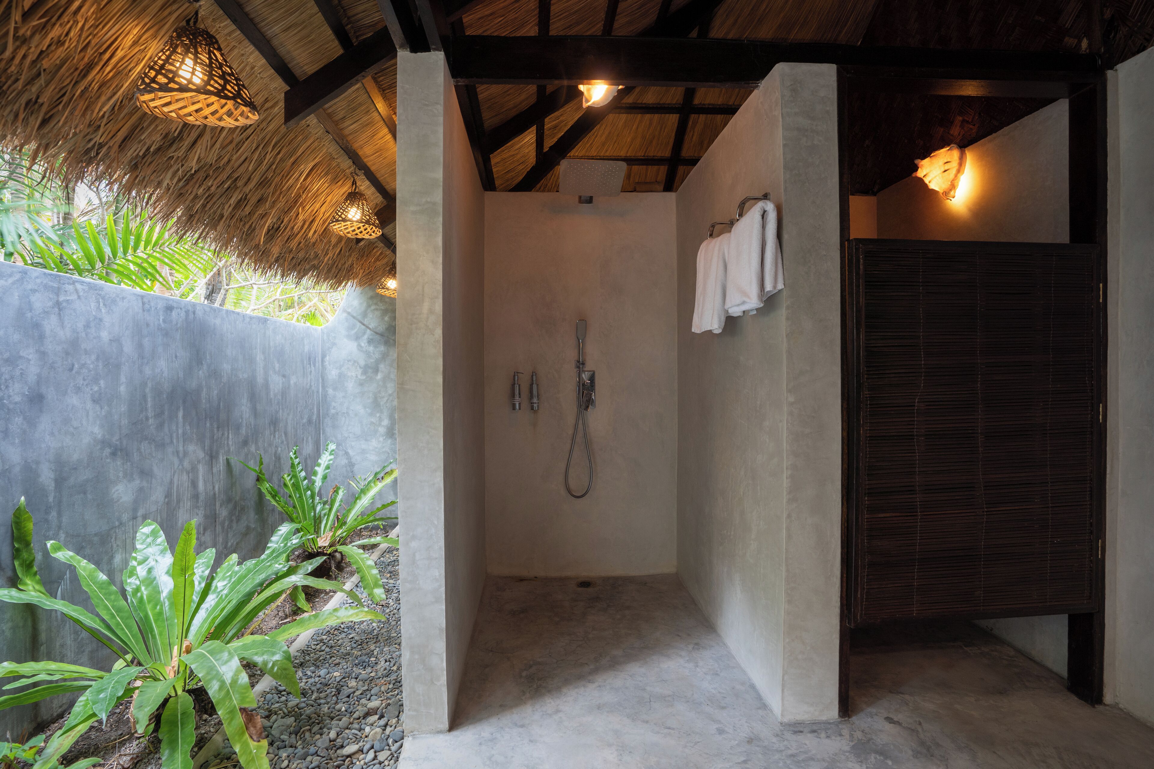 Zona de ducha con pared de concreto, techo de paja y un perchero para toallas.