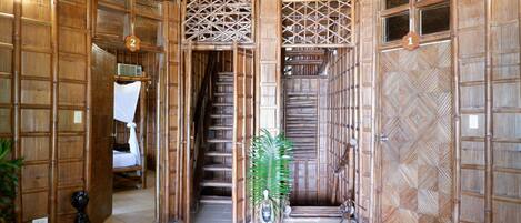 A traditional bamboo room with a bed, a small statue, and a decorative plant.