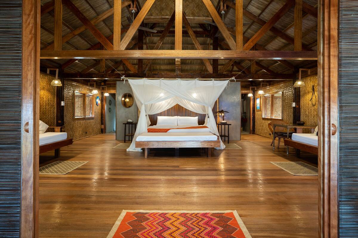 A spacious room with a large bed, wooden beams, and a thatched roof.