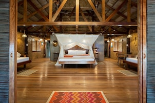 Amplia habitación con una cama grande, vigas de madera y techo de paja.