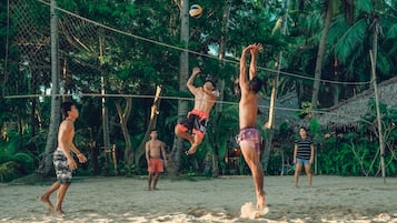 A group of people playing beach volleyball on a sandy court surrounded by lush greenery.