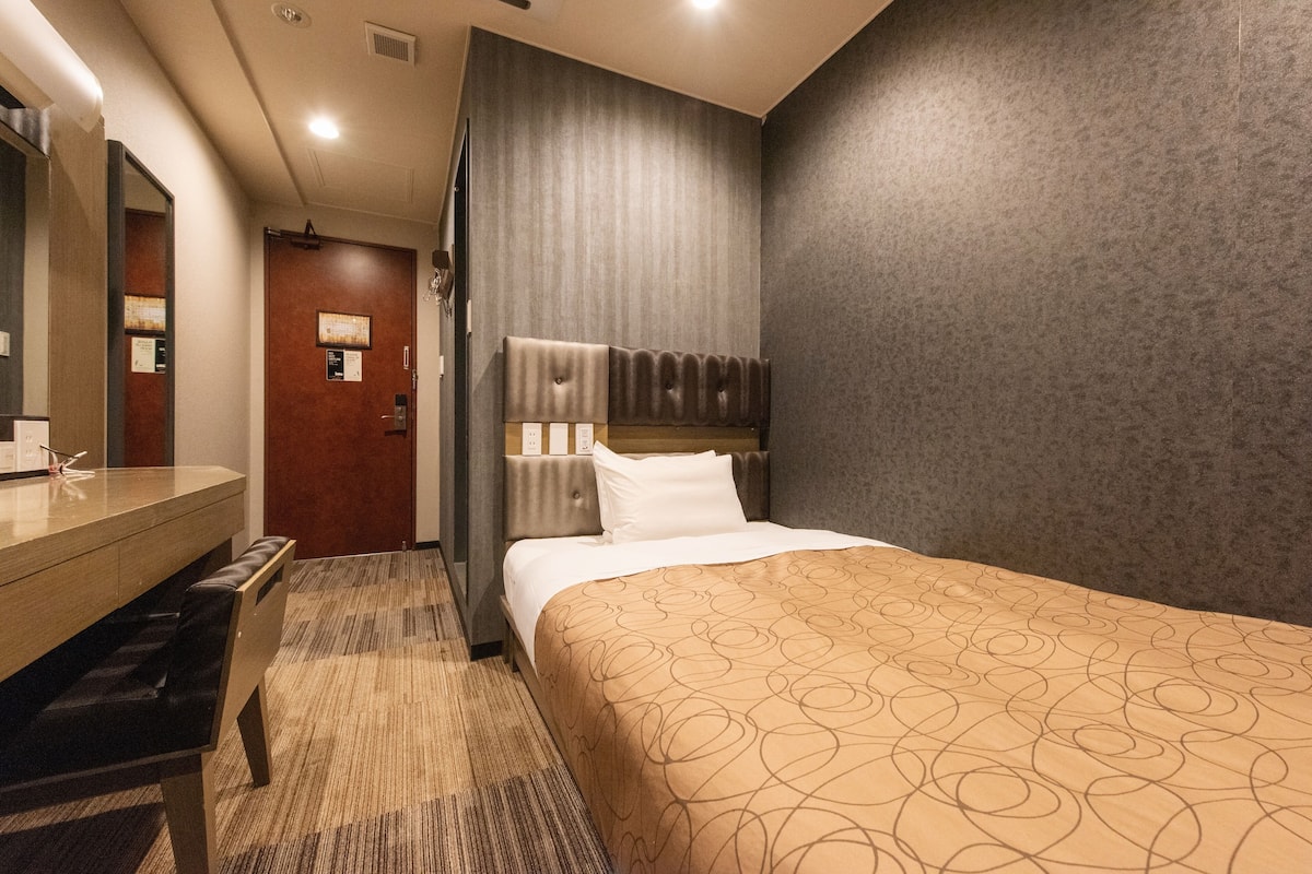 Une chambre d’hôtel avec un lit, un bureau avec une chaise, un miroir et une porte.