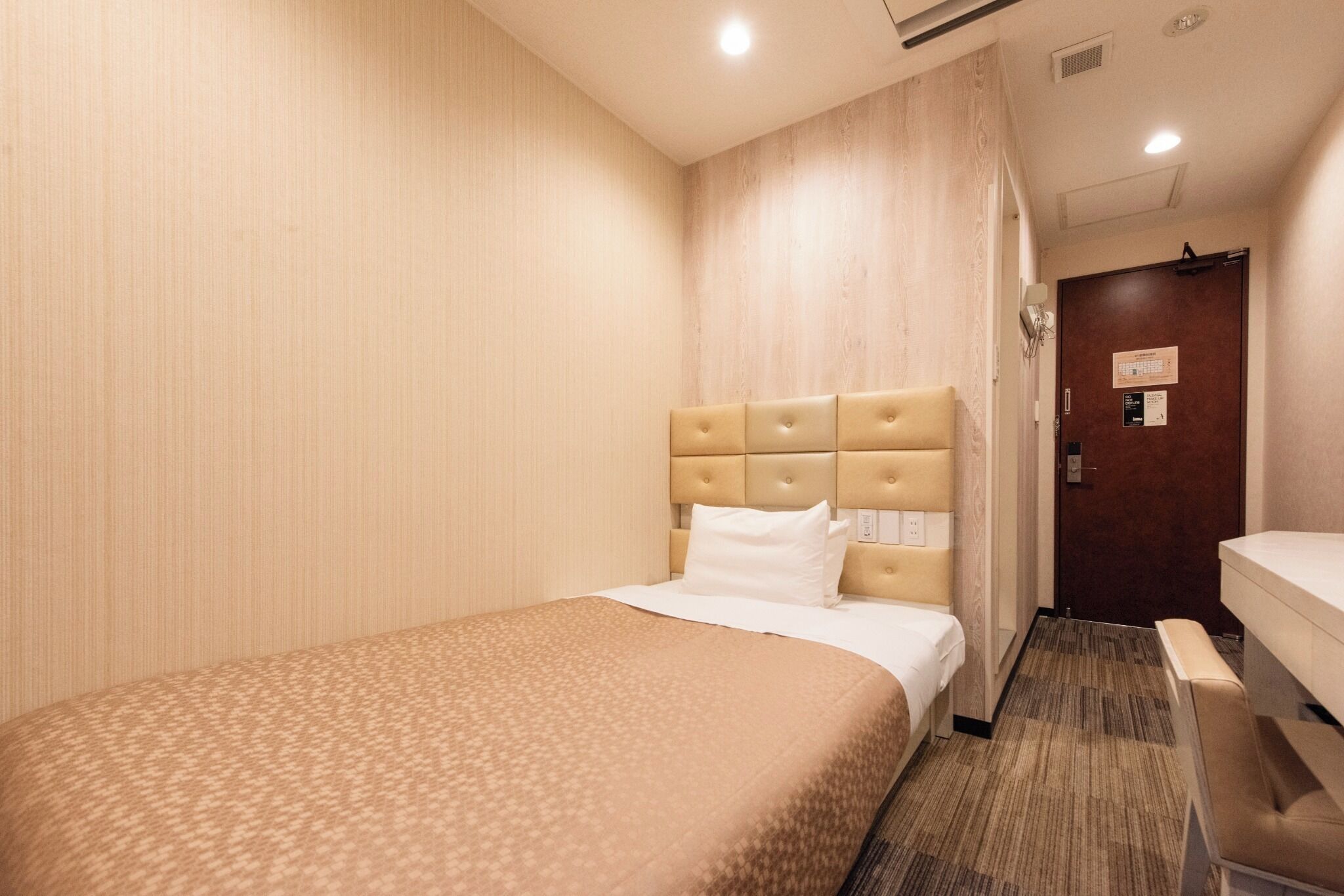A hotel room with a bed, a bedside table, a chair, and a door.