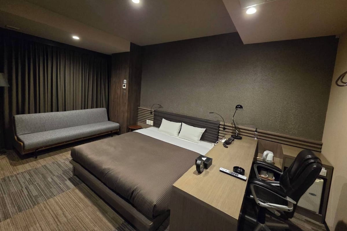 Une chambre d’hôtel avec un lit, un bureau, une chaise, un canapé et une grande fenêtre.