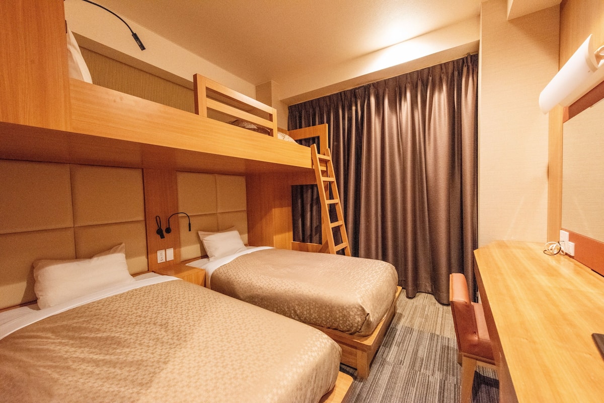 Une chambre d’hôtel avec deux lits simples, un lit superposé, un bureau et une chaise.