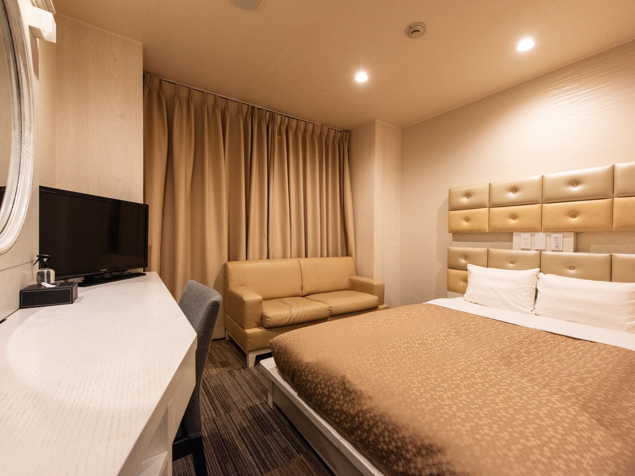 A hotel room with a bed, a desk, a chair, and a television.
