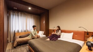 A hotel room with a large bed, a smaller sofa, a desk with a lamp, and a window with curtains. - Hotel Relief Sapporo Susukino (Sapporo)