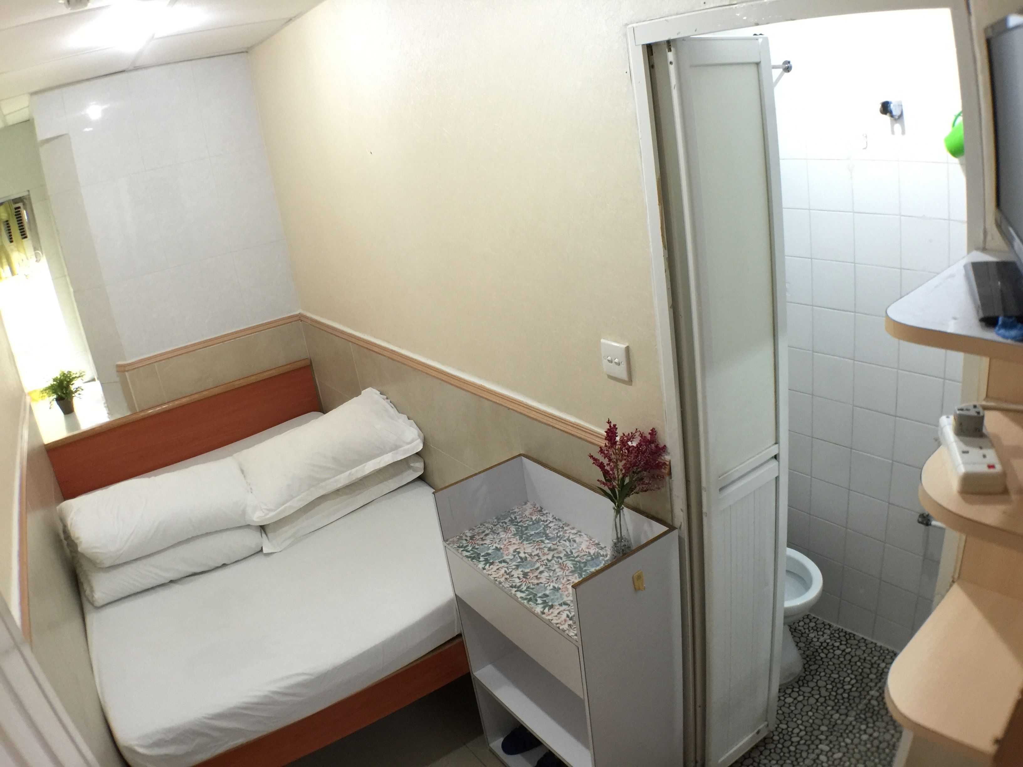 A small, compact room with a bed, a shower, and a toilet.