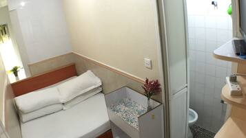 A small, compact room with a bed, a shower, and a toilet.