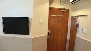 A bathroom with a wooden door, a wall-mounted TV, a towel rack, and a fire door sign. - Well Yet Guest House (Kowloon)
