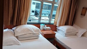 A hotel room with two beds, a window with curtains, a bedside table with a tissue box, and a wall-mounted light. - Well Yet Guest House (Kowloon)