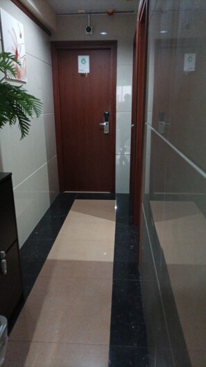 A hallway with a wooden door, a potted plant, and a tiled floor. - Well Yet Guest House (Kowloon)