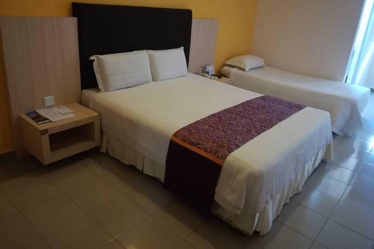 Une chambre d’hôtel avec un grand lit, un lit plus petit, une table de chevet et une commode.