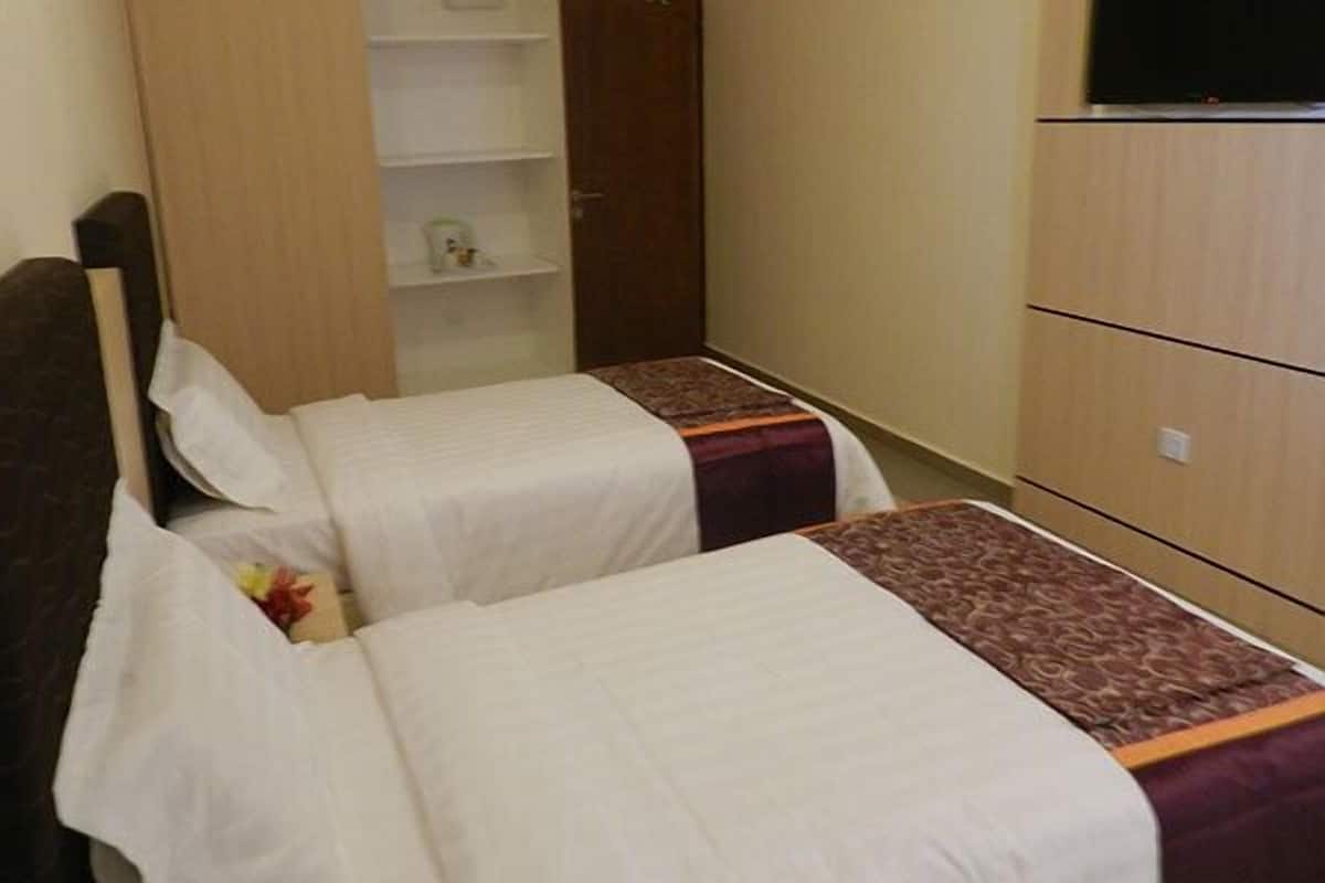 Une petite chambre d’hôtel avec deux lits simples, une armoire et un téléviseur.