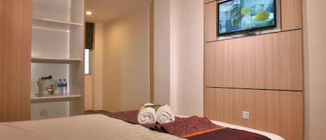 A hotel room with a bed, a television mounted on the wall, and a wooden wardrobe.
